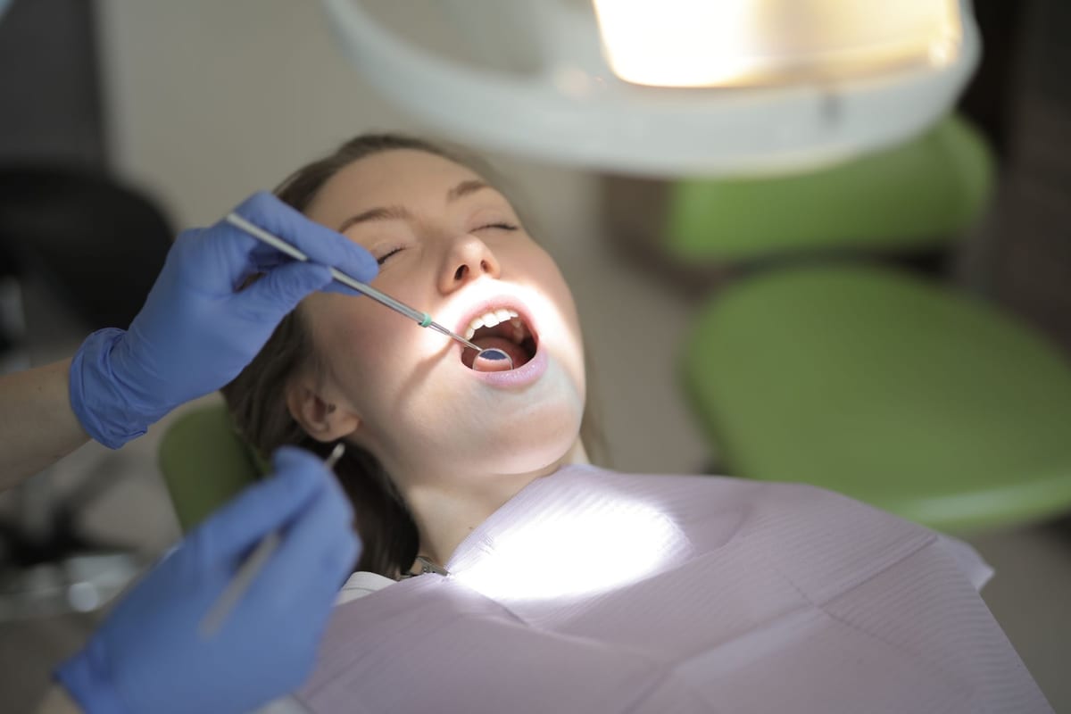 A dentist checking a patient's teeth with a mouth mirror under the chair light