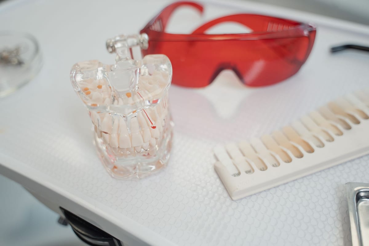 A clear dental model, a shade guide and safety glasses on a clinic tray