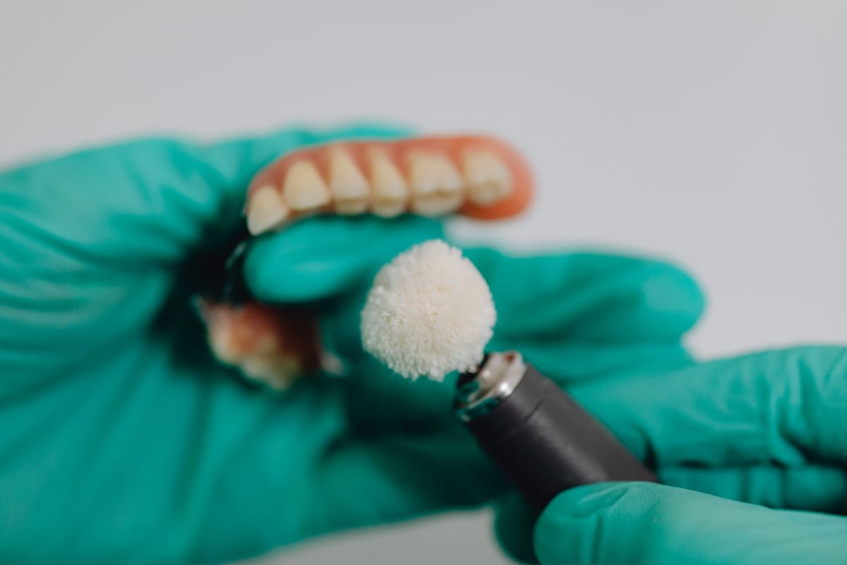 Gloved hands polishing a denture with a rotary brush